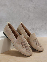Beige gebreide instappers met gaatjesmesh, een schoen leunend tegen een wit blok voor een grijze muur. 7