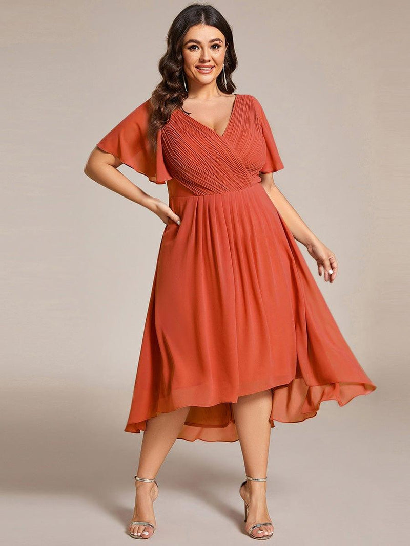 Model met ruimere maat in terracotta chiffon jurk met V-hals, fladdermouwen en wijd uitlopende hoog-laag rok. 97
