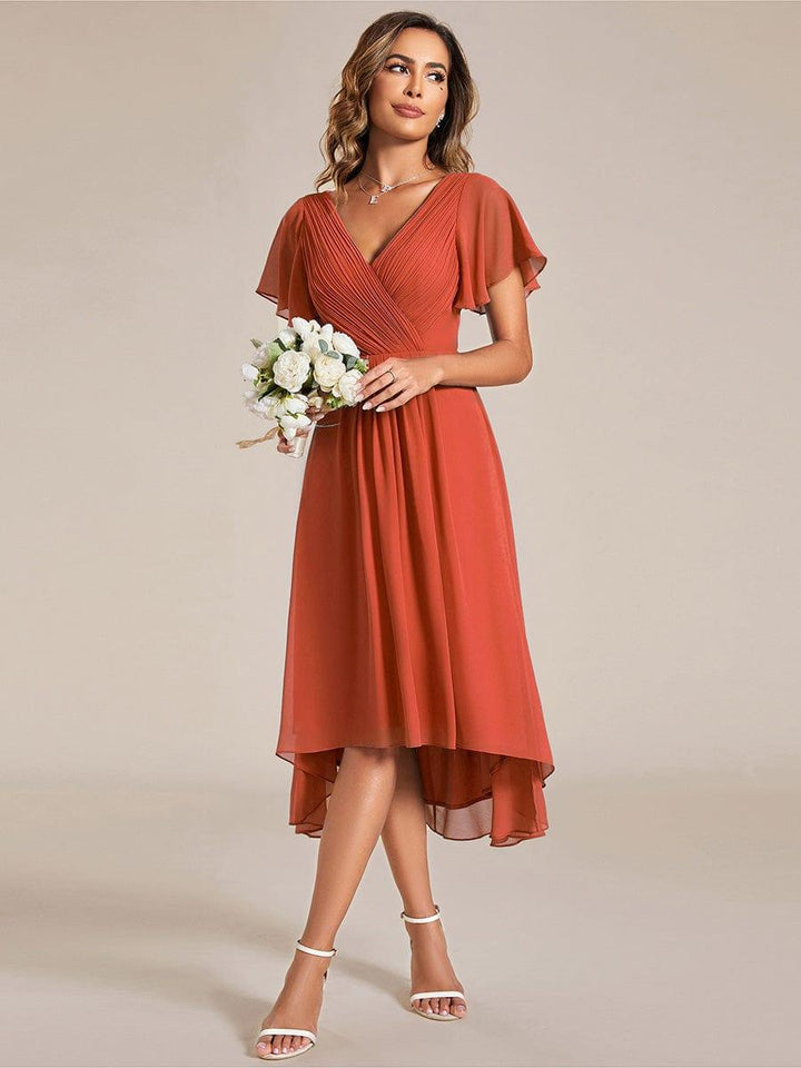 Model in terracotta jurk houdt een klein boeket witte bloemen vast, de hoog-laag zoom valt luchtig. 95