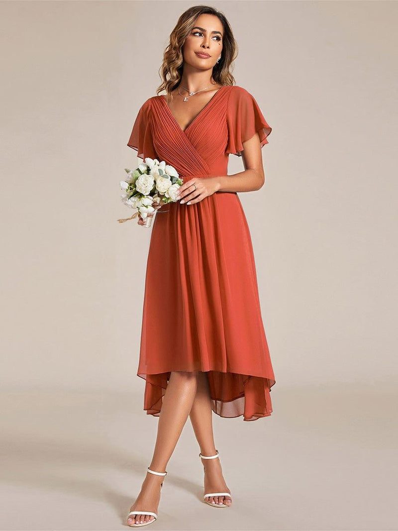 Model in terracotta jurk houdt een klein boeket witte bloemen vast, de hoog-laag zoom valt luchtig. 95