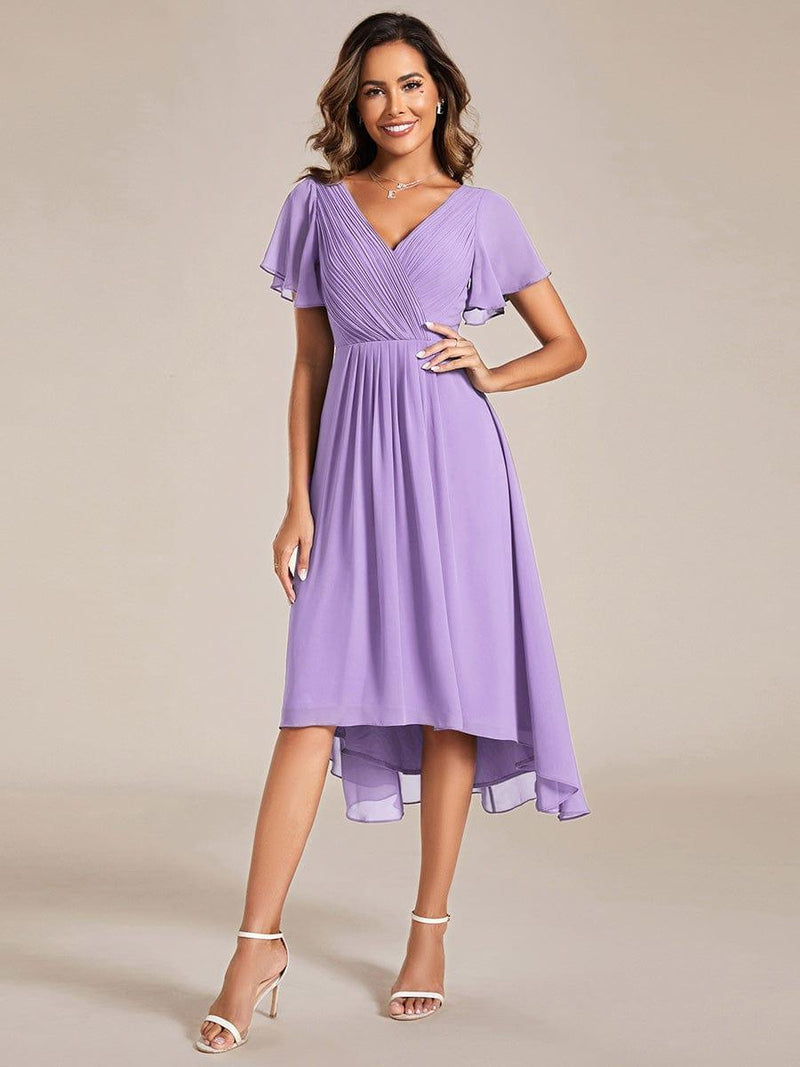 Model in lila chiffon jurk met gekruiste geplooide V-hals, fladdermouwen en hoog-laag zoom, witte sandalen. 100