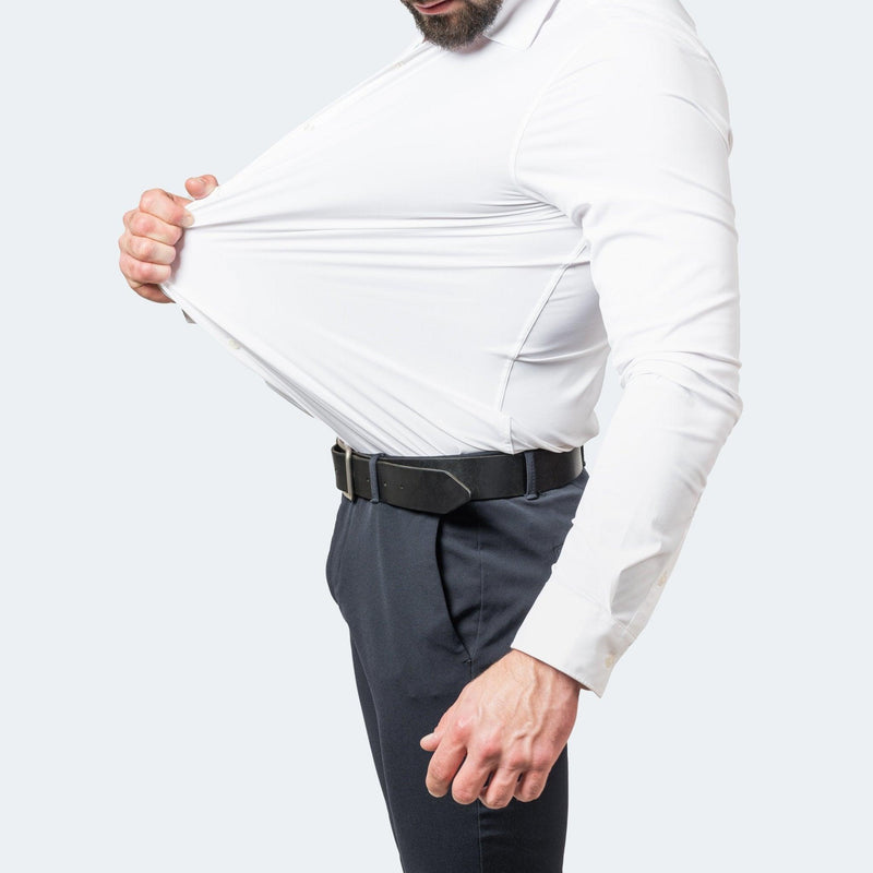 Wit overhemd gedragen met donkere pantalon en zwarte riem, terwijl de man de stof aan de voorkant ver uitrekt. 3