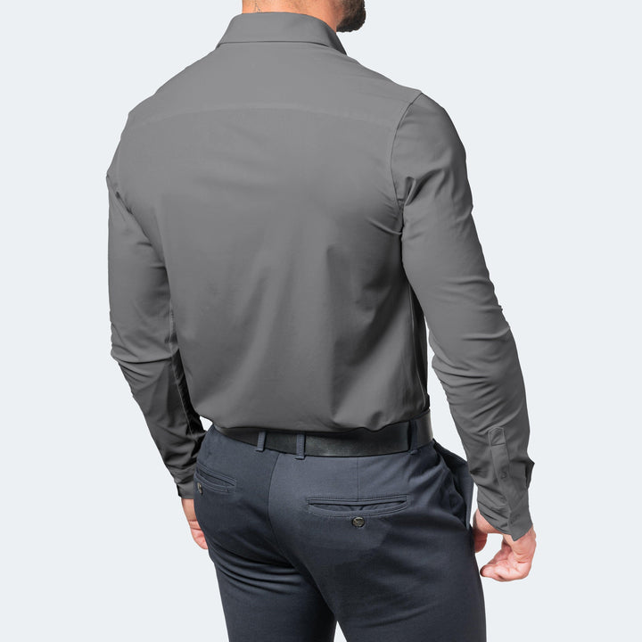 Achterkant van een grijs overhemd met lange mouwen, gedragen door een man in een donkerblauwe pantalon met zwarte riem. 6