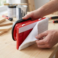 Handen bevestigen een wit pad op de klittenbandzijde van het rode gereedschap, op een houten werkbank met verfblikken erachter. 3