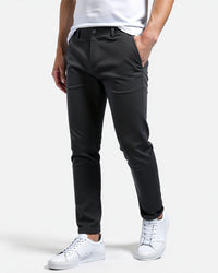 Donkergrijze slim fit chino van opzij gedragen met wit shirt en witte sneakers, een hand in de zak. 12