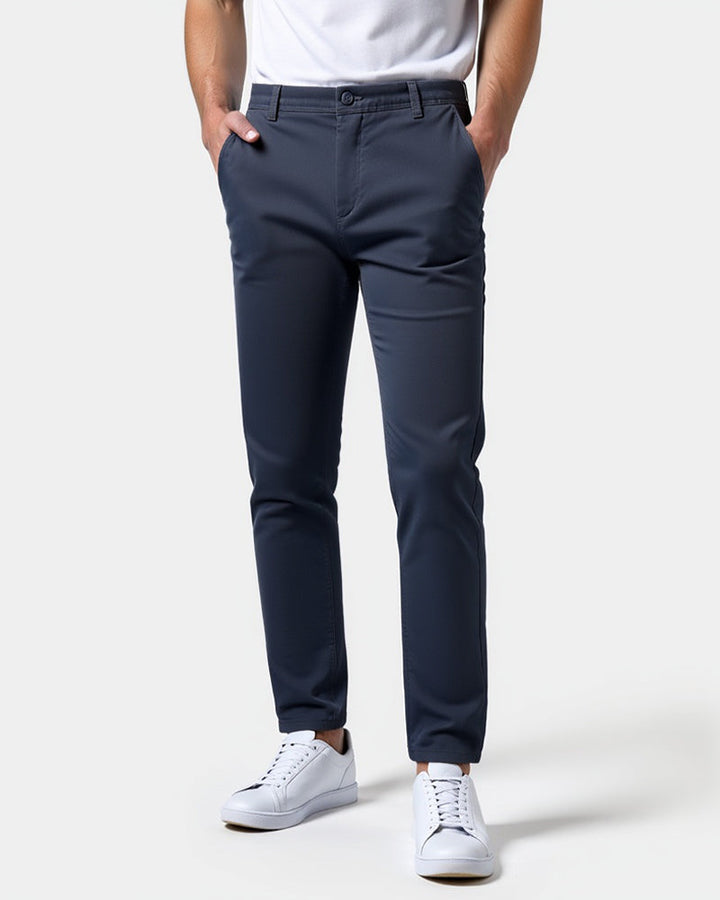 Donkerblauwe slim fit chino van voren gedragen met wit shirt en witte sneakers, beide handen in de zakken. 15