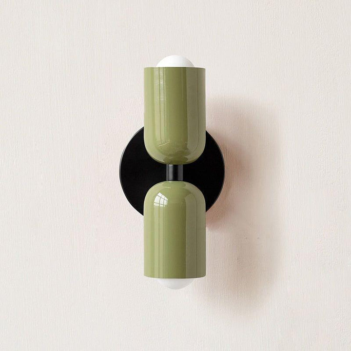 Wandlamp met twee groene lampkoppen boven elkaar op een ronde zwarte muurplaat tegen een lichte muur. 10