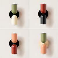 Collage van vier wandlampen met twee lampkoppen in verschillende kleurcombinaties van groen, crème, rood, zwart en perzik op een lichte muur. 1