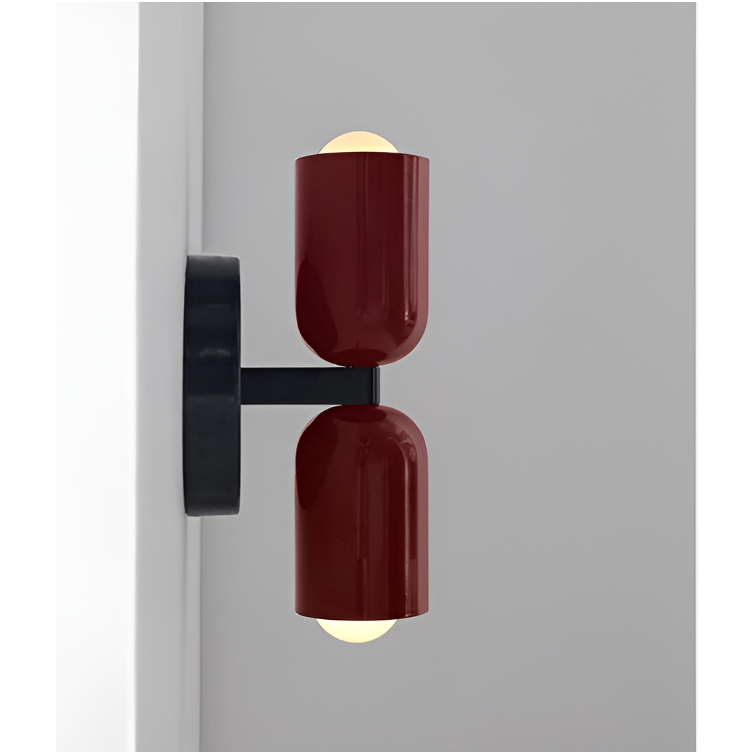 Zijaanzicht van een wandlamp met twee rode lampkoppen op een zwarte arm en ronde zwarte muurplaat, de peertjes lichten warm op. 17