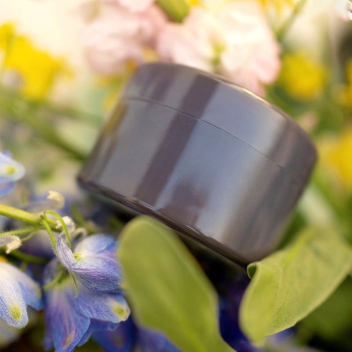 Donkergrijze ronde inzet glanst tussen blauwe, gele en roze bloemen en groene bladeren. 10