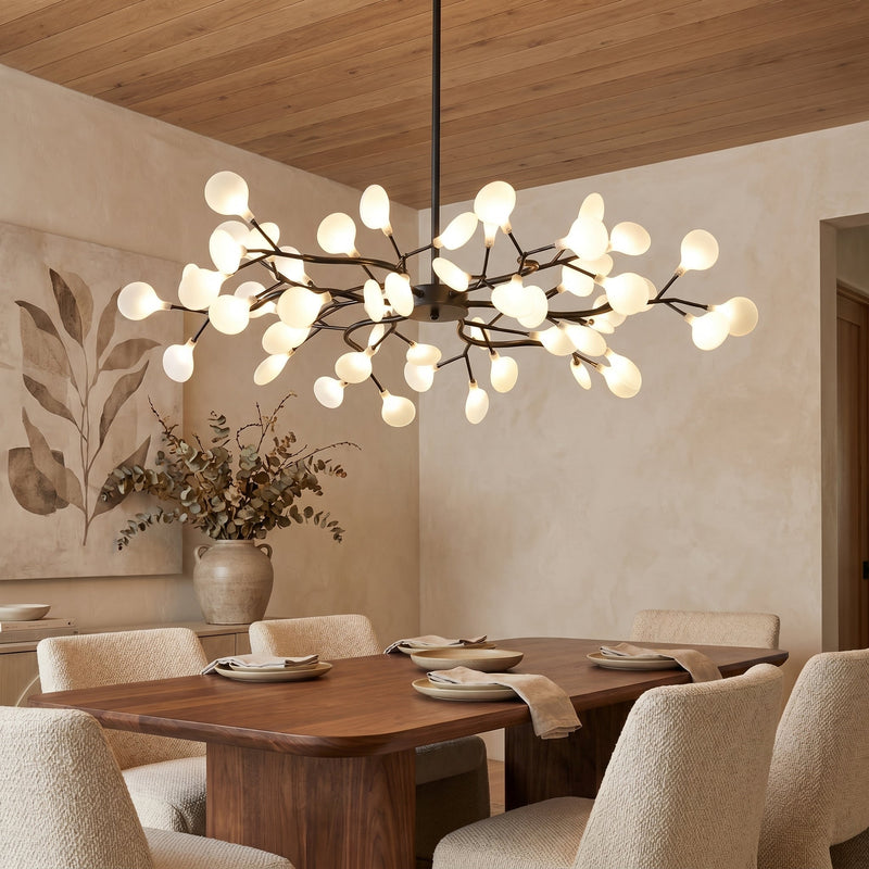 Zwarte takkenlamp met matwitte bollen boven een houten eettafel met beige stoelen en eucalyptustakken 1