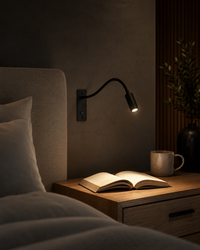 Zwarte wandlamp werpt een warm lichtkegel op een opengeslagen boek op een houten nachtkastje, naast een beige mok in een donkere slaapkamer. 6