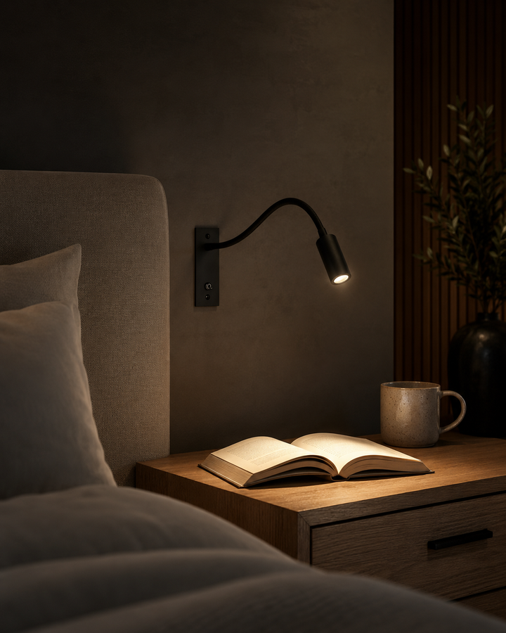 Zwarte wandlamp werpt een warm lichtkegel op een opengeslagen boek op een houten nachtkastje, naast een beige mok in een donkere slaapkamer. 6