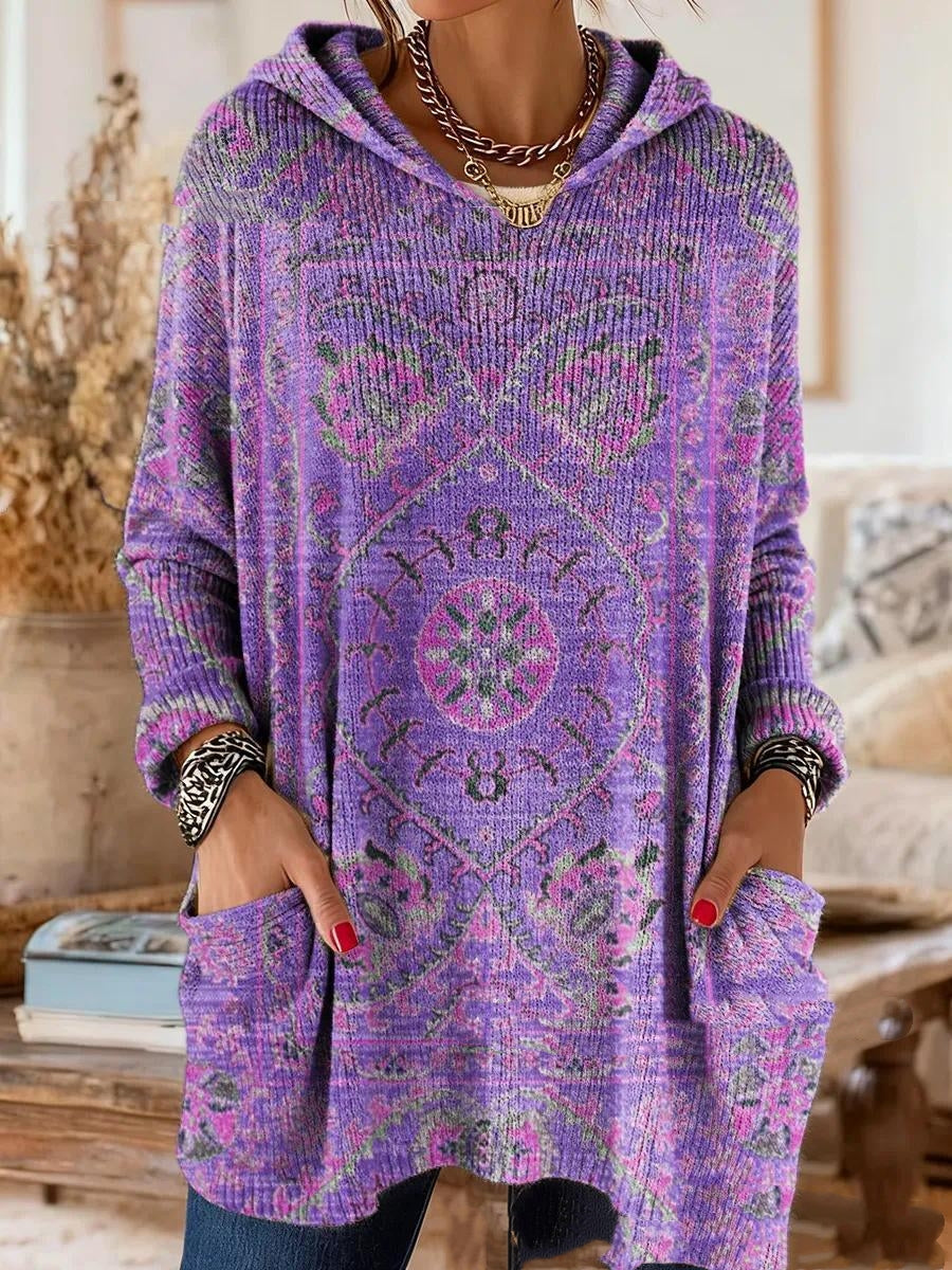 Dezelfde tuniek met capuchon in paars met roze en groene tapijtprint, gedragen met handen in de voorzakken. 2