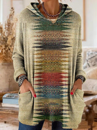 Tuniek met capuchon in zandkleur met een verticale geometrische print in groen, rood en blauw, gedragen met handen in de zakken. 5