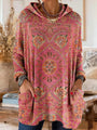 Roze tuniek met capuchon en oranje en groene tapijtprint, gedragen door een model met handen in de voorzakken. 6