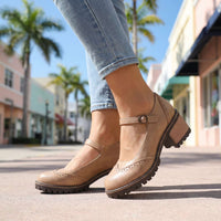 Beige Mary Jane-schoenen met bandje en brogue-perforatie vanuit lage hoek gefotografeerd op een zonnige winkelstraat 9