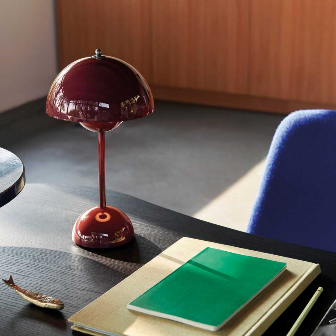 Glanzend bordeauxrode lamp op een donker bureau naast notitieboeken en een blauwe stoel 18