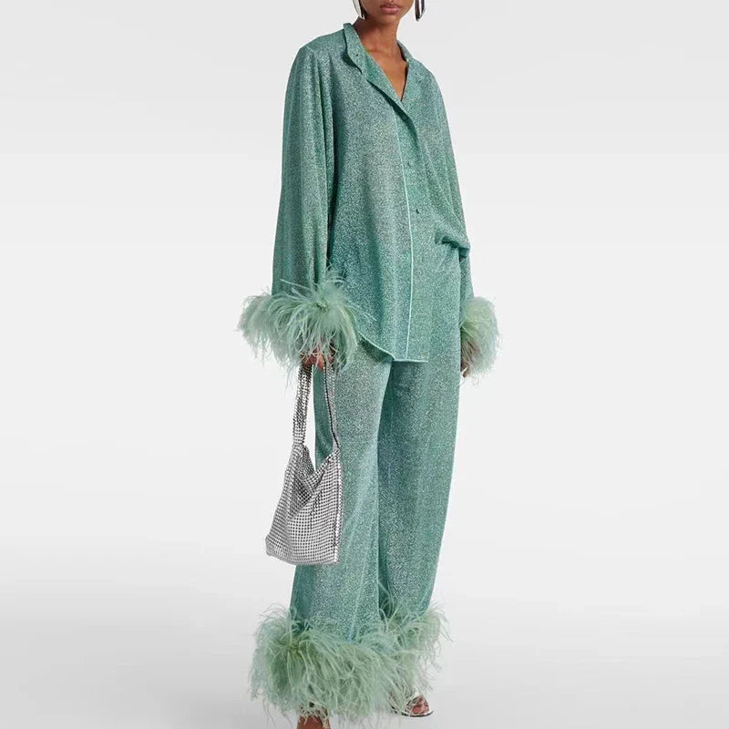 Model draagt de glitterset in mintgroen met reverskraag en veren aan manchetten en pijpen, met een zilverkleurige tas in de hand. 2