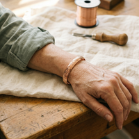 Gegraveerde koperen armband om de pols van een model dat de arm op een houten tafel legt 2