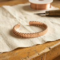 Open koperen armband met overlappende schijven op linnen doek naast een koperdraadspoel en gereedschap 1