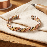 Open gevlochten armband van koper, messing en zilverkleurig metaal op linnen doek naast een rol koperdraad 1