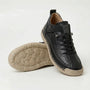 Zwarte sneaker met opvallende handgestikte rand en beige zool, met de noppenzool van de tweede schoen in beeld. 12