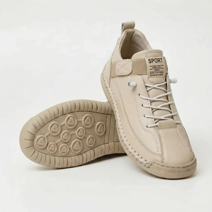 Crèmekleurige sneaker met witte elastische veters en tonale zool, naast een schoen met de noppenzool naar boven. 10