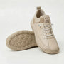 Crèmekleurige sneaker met witte elastische veters en tonale zool, naast een schoen met de noppenzool naar boven. 10