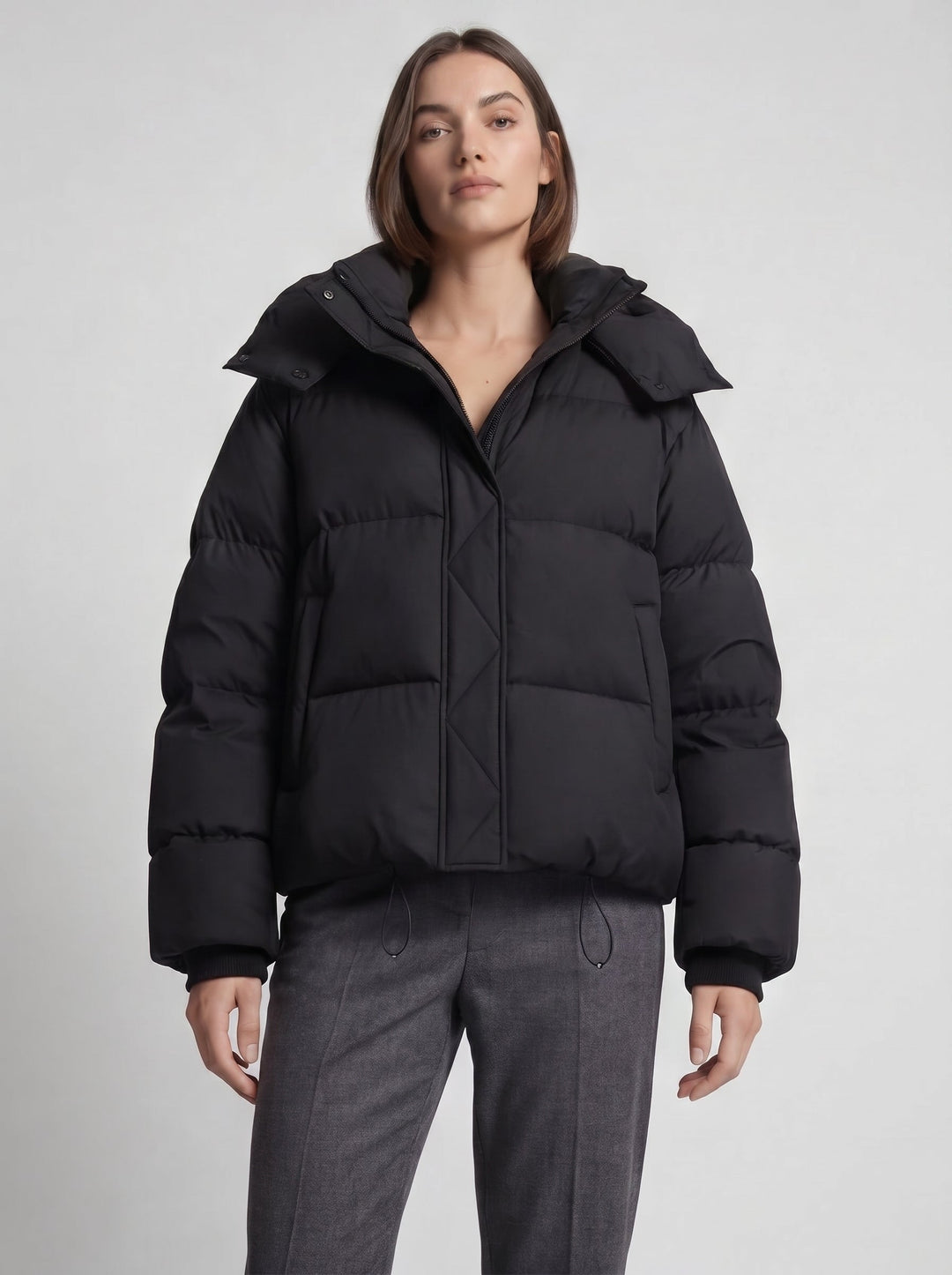 Model draagt de zwarte oversized gewatteerde jas dichtgeritst met capuchon, halve lengte vooraanzicht 6