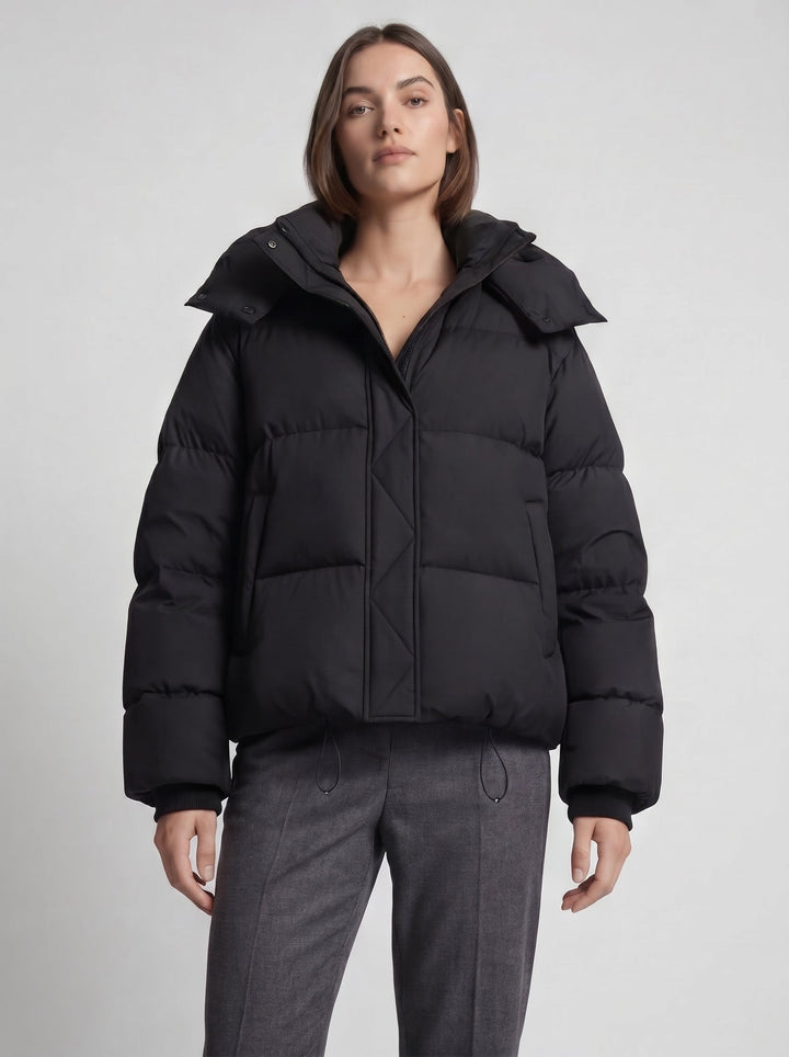 Model draagt de zwarte oversized gewatteerde jas dichtgeritst met capuchon, halve lengte vooraanzicht 6