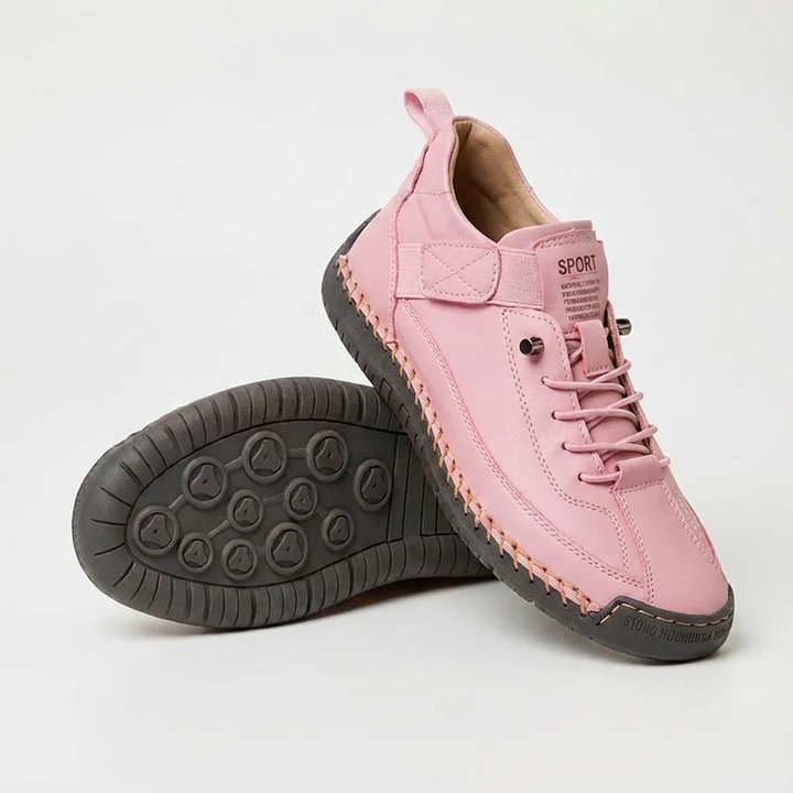 Roze sneaker met oranje stiksels en donkergrijze zool, met de tweede schoen op zijn kant en de zool zichtbaar. 14