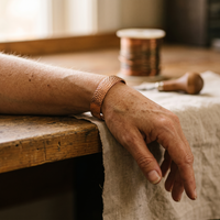 Koperen armband met hamerslagstructuur om een pols, rustend op een houten tafel 2