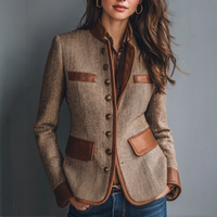 Voorkant van de tweedjas in visgraatpatroon, gedragen met bruine blouse en spijkerbroek, met leren klepzakken, metalen knopen en leren manchetten. 1