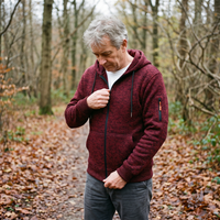 Man met grijs haar draagt de bordeauxrode hoodie en sluit de rits tijdens een wandeling in een herfstbos. 6