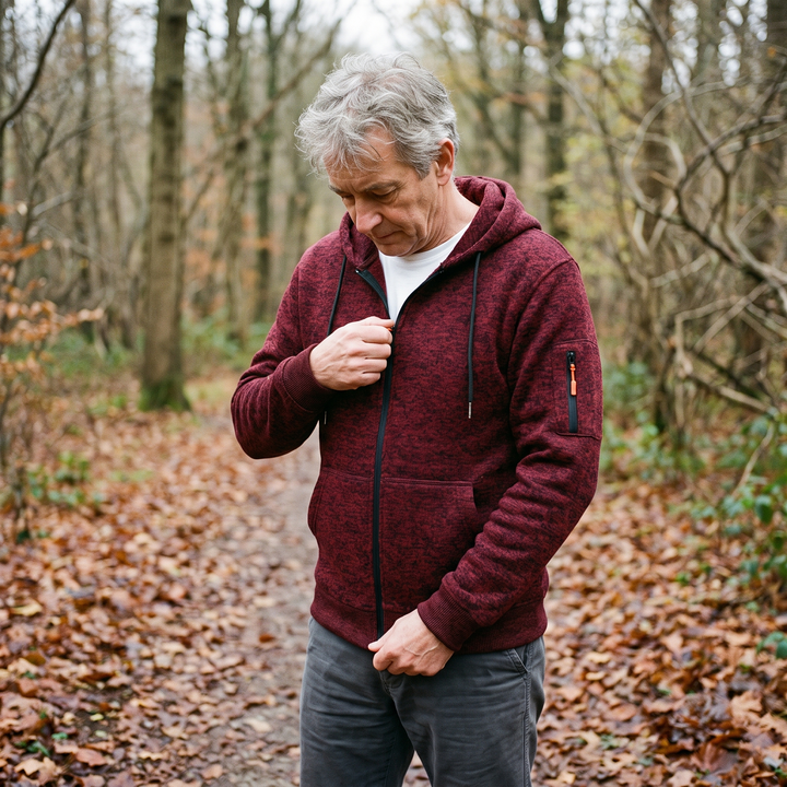 Man met grijs haar draagt de bordeauxrode hoodie en sluit de rits tijdens een wandeling in een herfstbos. 6