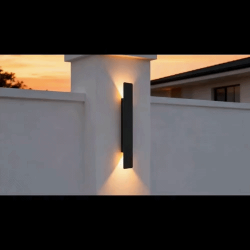 Zwarte wandlamp op een witte tuinmuurpijler tegen een oranje schemerlucht, met licht omhoog en omlaag 6