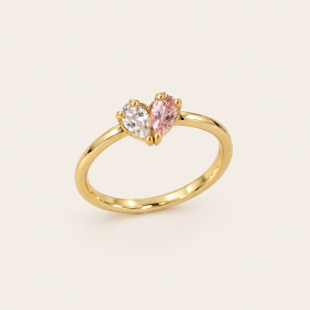 Gouden ring van schuin voren gezien met een helder en een roze druppelvormige steen die samen een hartje vormen. 1