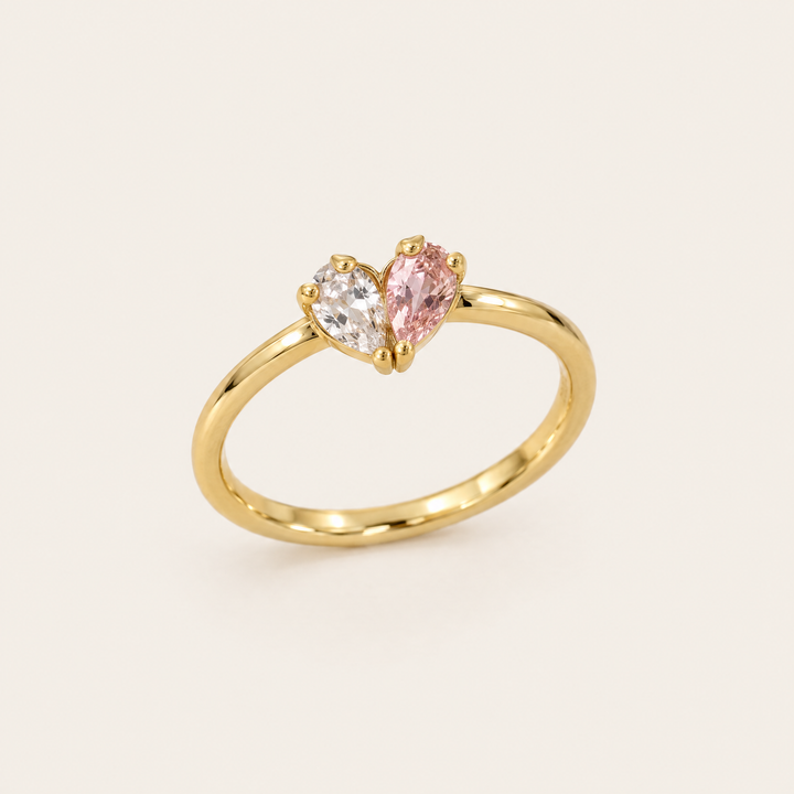 Gouden ring van schuin voren gezien met een helder en een roze druppelvormige steen die samen een hartje vormen. 1