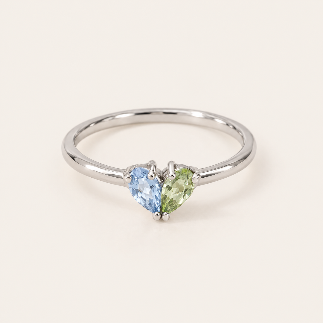 Zilverkleurige ring van voren gezien met een blauwe en een lichtgroene druppelvormige steen die samen een hartje vormen. 5