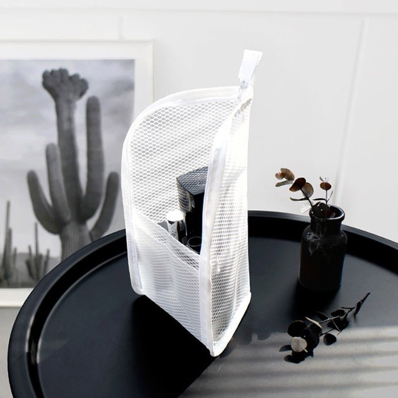 Witte mesh toilettas staat rechtop op een zwart tafeltje, gevuld met cosmetica, naast een vaasje met takjes en een cactusposter. 2