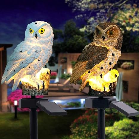 Een witte en een bruine verlichte uilenlamp naast elkaar op palen met zonnepaneel, 's avonds in de tuin. 17