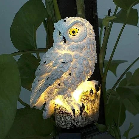 Close-up van een lichtgevende witte uil met gele ogen en zwarte stippen, tussen grote groene bladeren. 8