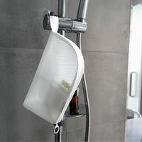 Witte mesh toilettas hangt aan de lus aan de douchestang in een betegelde douche, met flesjes in de buurt. 4