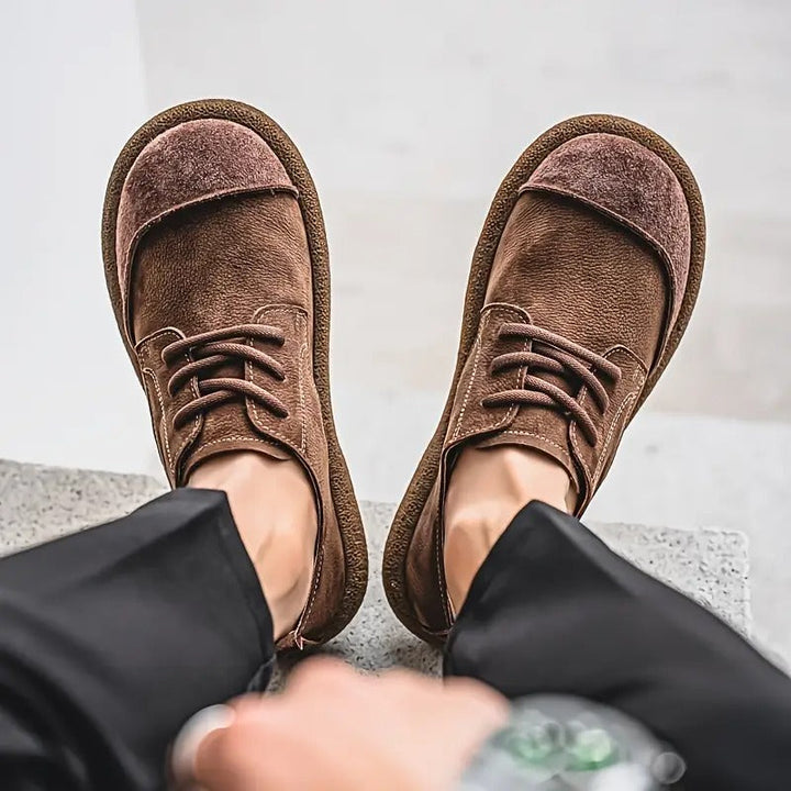 Dragersperspectief van boven op twee voeten in donkerbruine veterschoenen met brede neus, onder een zwarte pantalon. 8