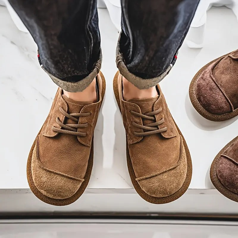 Bovenaanzicht van twee voeten in bruine veterschoenen met opgerolde donkere broekspijpen, naast een paar donkerder bruine schoenen. 4