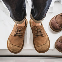 Bovenaanzicht van twee voeten in bruine veterschoenen met opgerolde donkere broekspijpen, naast een paar donkerder bruine schoenen. 4
