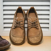 Paar lichtbruine veterschoenen van voren tegen een lamellenpaneel, met aan de zijkant een donkere schoen. 9