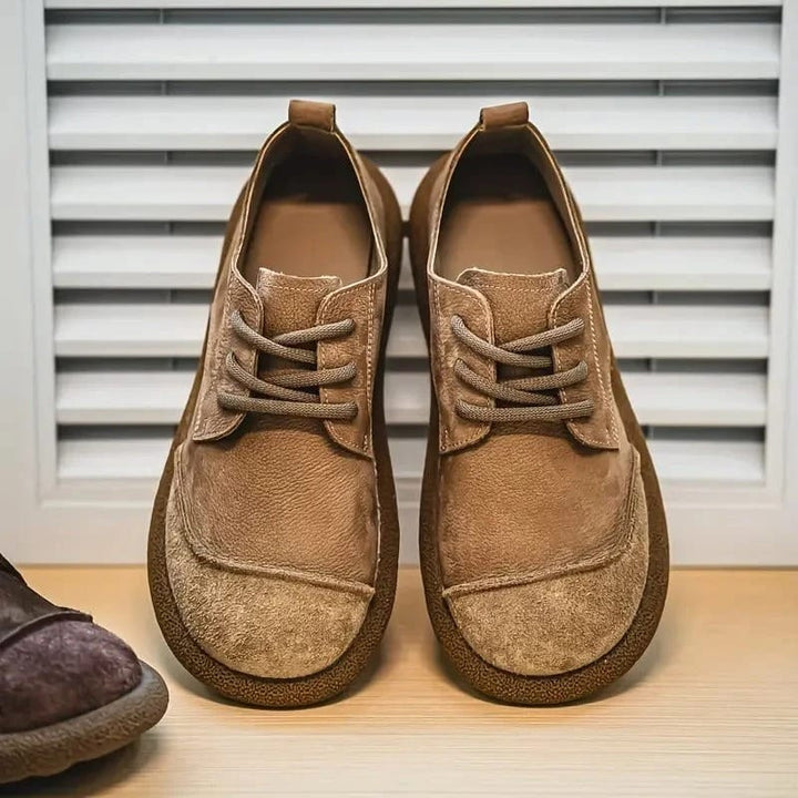 Paar lichtbruine veterschoenen van voren tegen een lamellenpaneel, met aan de zijkant een donkere schoen. 9
