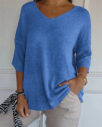 Model draagt blauwe pullover met V-hals en geribbelde mouwboorden, gecombineerd met beige broek en gouden kettingen 1